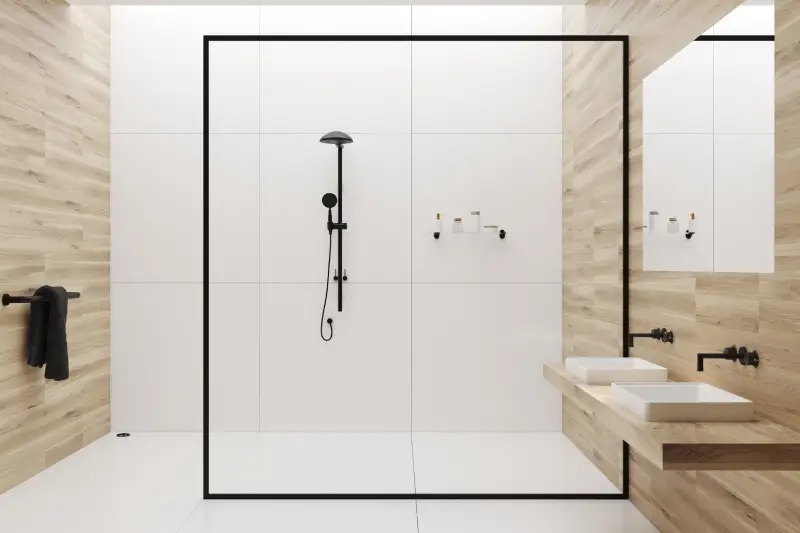 White tiles and wooden bathroom interior with a tiled white floor, a sink with a mirror above it, a black towel in the corner and a black shower behind a glass wall.